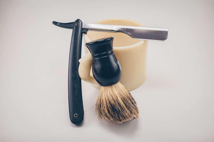 how long does a shaving brush last: black straight razor beside beige ceramic mug and shaving cream brush