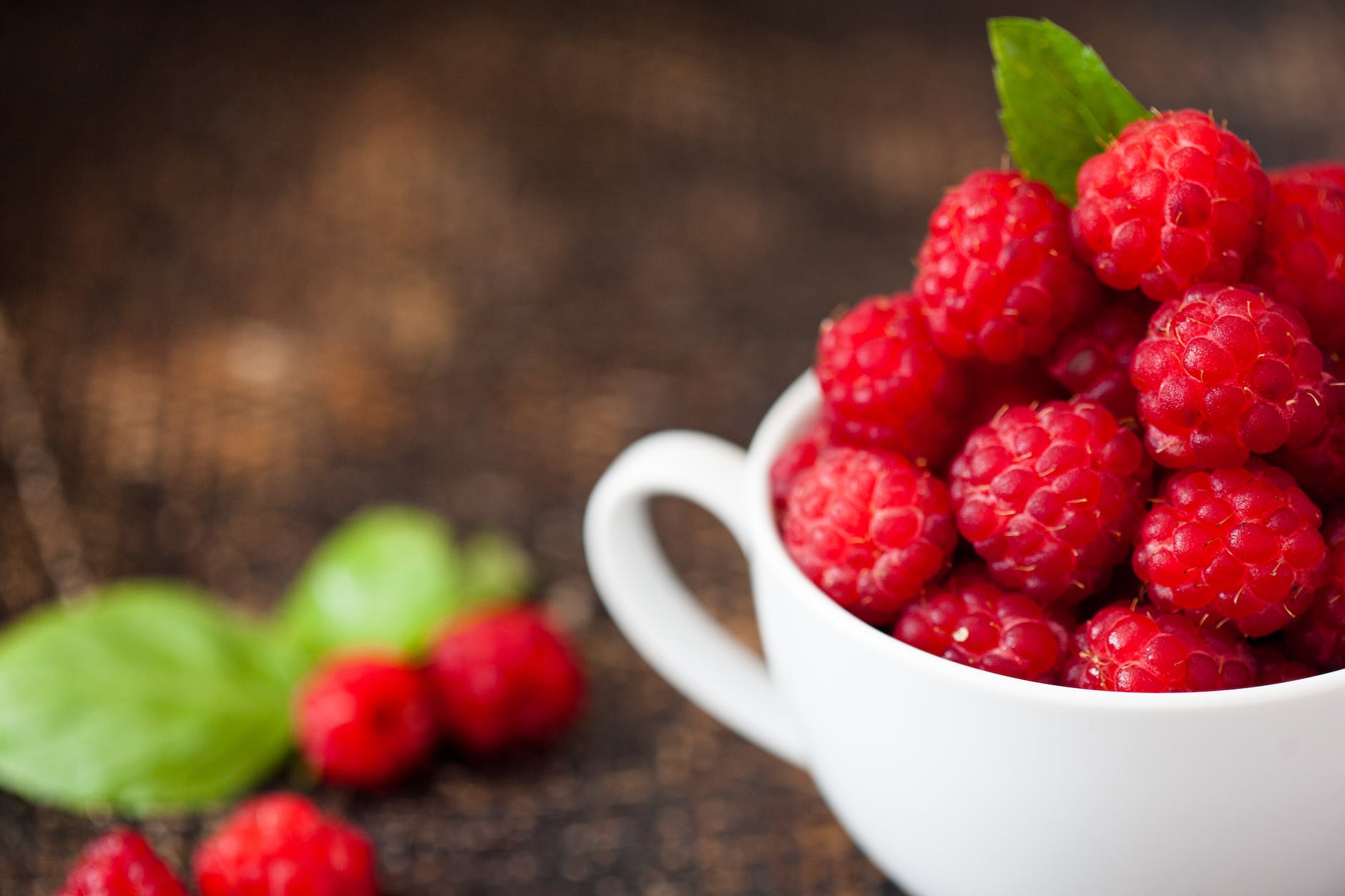 ripe raspberries in white teacup in tilt shift photography